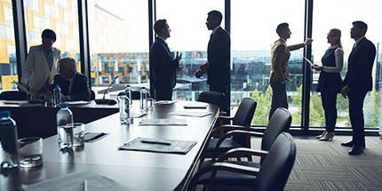 image of a group of business people in conversation standing in a spacious conference room with floor to ceiling windows