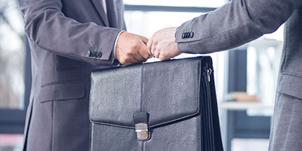 a close up of two men in business suits - one is passing a briefcase to the other